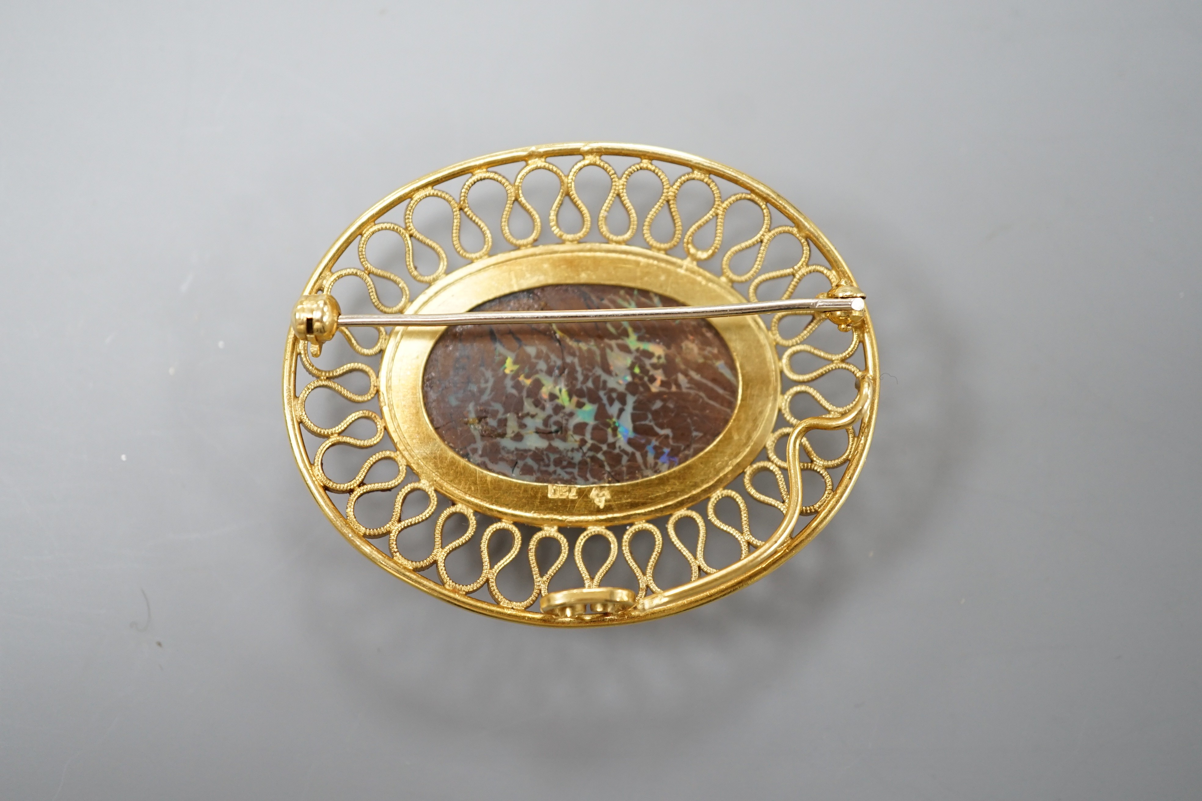 A continental 750 yellow metal and large oval boulder? opal set pendant brooch, with a filigree scroll border, 47mm, gross weight 20 grams (opal cracked).